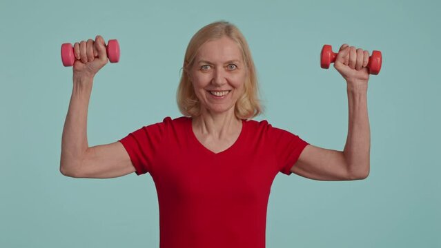 Active senior woman posing with dumbbells in hands and siling . studio shot 