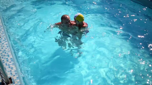 Grandpa teaches granddaughter to swim in swimming pool