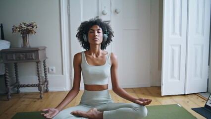 Tranquil lady meditating on carpet zoom out. African woman sitting lotus pose