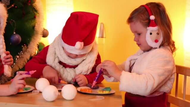 Three children paint on cookies near christmas tree