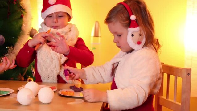 Two girls and boy paint on cookies near christmas tree