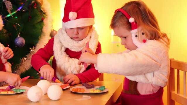 Two little girls and boy paint on cookies near christmas tree