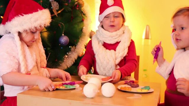 Two little girls and boy show colored cookies near christmas tree