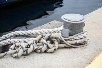 Fototapeta na wymiar Metal dock mooring pole with rope for securing fishing boats closeup