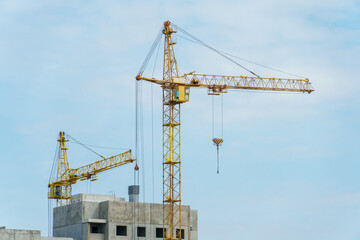 Silhouettes of working construction cranes against the background of an unfinished residential building. Multi-storey luxury apartment building on a construction site