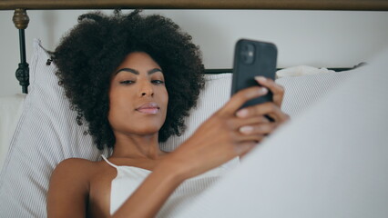 Sensual woman resting cellphone bed. Portrait african curly lady looking camera