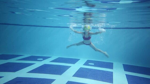 Girl in goggles swim underwater in empty indoor pool