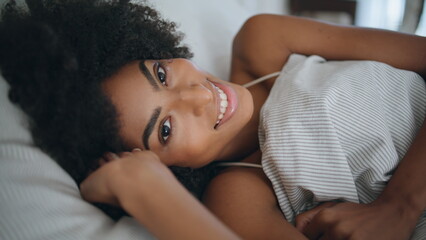 Happy lady wakeup bedroom portrait. African woman looking camera lying bed alone