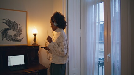 Carefree lady dancing at home. Headphones african woman listening music at house