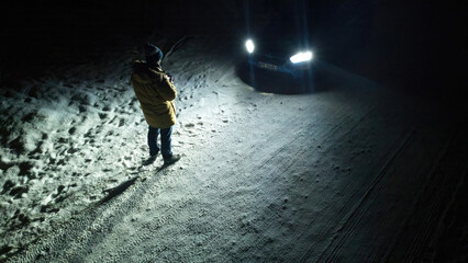 A man standing in the light of car headlights, winter conditions and snow on slippery road, concept...