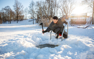 Man carving out a hole in the ice with an axe for winter swimming in cold sunny winter day