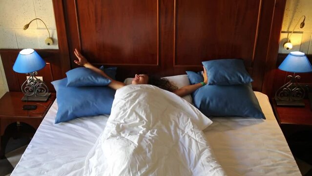 Pretty woman awakes on wooden double bed with white linen