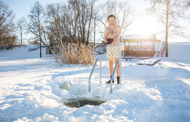 Confident man emerging from an ice swimming hole in winter, clad in swim shorts against snowy...