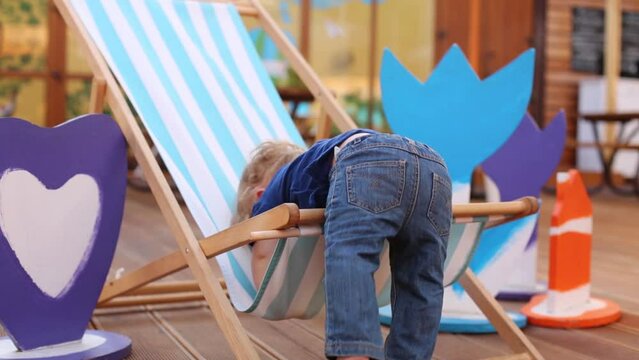 Little boy tries to get out of sun lounger in cafe with veranda