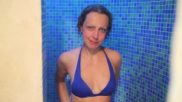 Pretty woman in swimsuit takes shower with blue tiling
