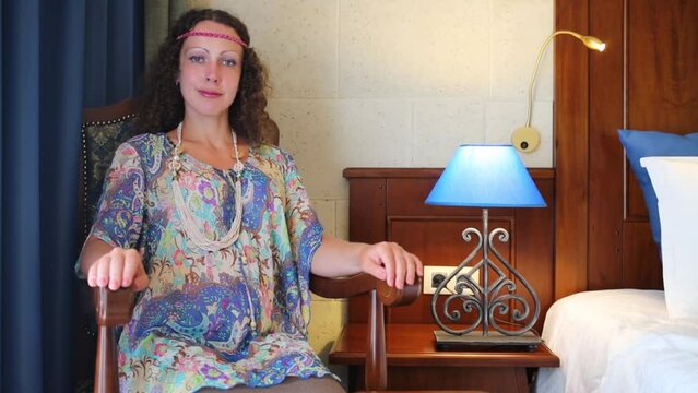 Pretty woman in ethnic dress sits near blue lamp in hotel room