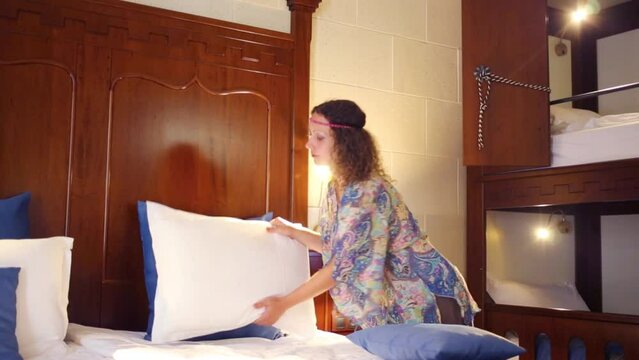 Pretty woman corrects pillows on double bed in hotel room