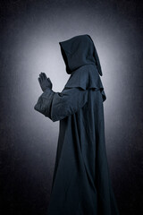 Medieval monk in hooded cloak praying in the dark