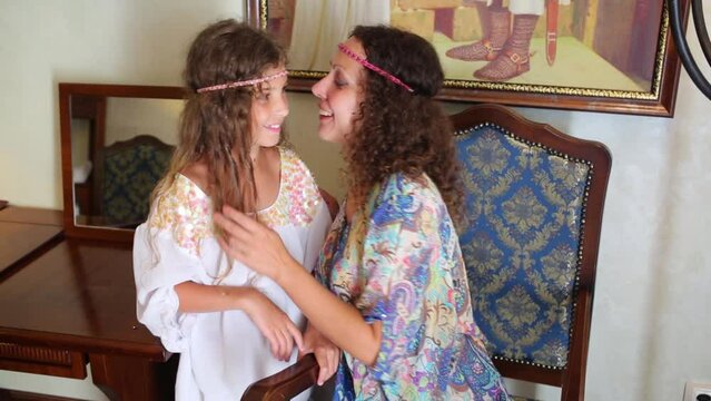 Mother and daughter in ethnic dresses whisper in room