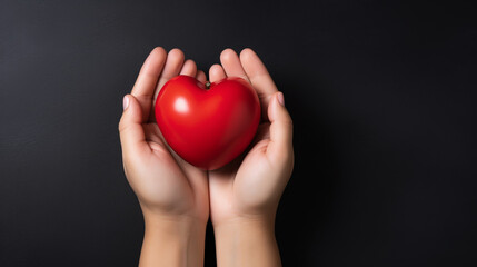 Top view photo of hands holding red heart on black background, healthcare, love, organ donation, mindfulness, wellbeing, family insurance and CSR concept, World Heart Day.