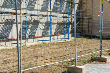 Scaffolding is installed along the wall of the building under construction. Plastering and painting...