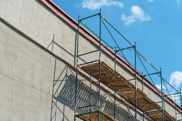 Scaffolding is installed along the wall of the building under construction. Plastering and painting of the facade of the house. Metal supports and wooden platforms for working at height.