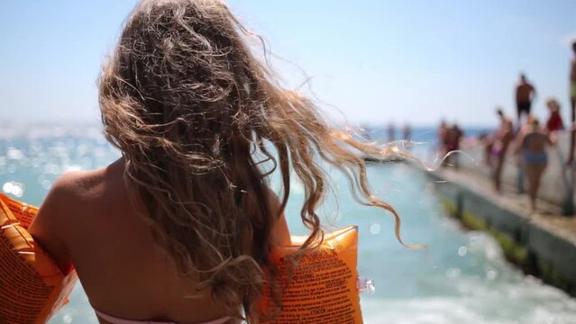 Back of girl in swimsuit and inflatable armbands going to sea