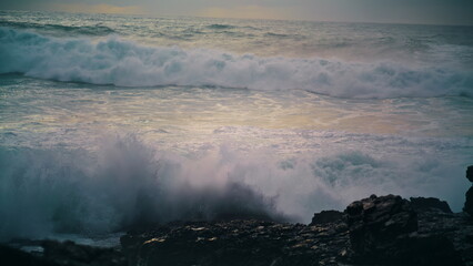 Fototapeta premium Foaming waves breaking coastline stones close up. Powerful ocean rolling shore