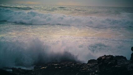 Foaming waves breaking coastline stones close up. Powerful ocean rolling shore