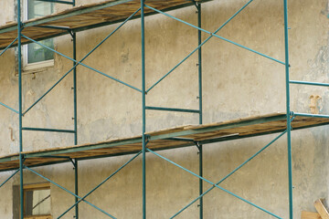 Scaffolding is installed along the wall of the building under construction. Plastering and painting...
