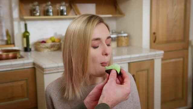 Close up. A man's hands hold a green mochi cake and give it to a young blonde woman to bite. She tastes with an emotion of pleasure. The concept of a romantic meeting with dessert.