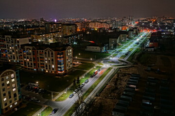 The lights of the night city. View of the busy city traffic and the light from the headlights of cars at night. The lights are on in the windows of residential buildings.