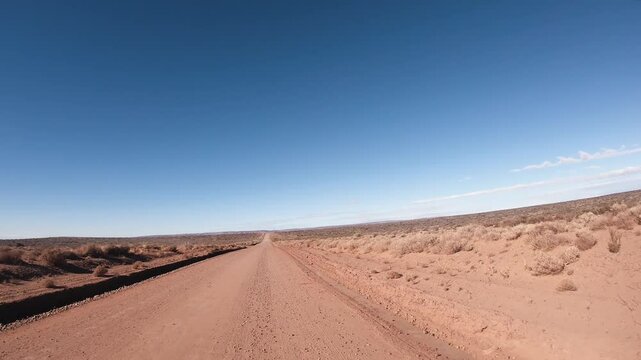 Traveling in the oilfields of Vaca Muerta. Point of view of a car driving along the desert road under a clear blue sky. 
