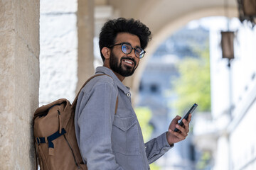 Smiling dark-haired man standing in the arch with a phone in hand