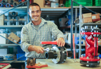 Positive caucasian man mechanic assembling plumbing fixture in workshop.