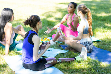Multiracial group of college friends sitting on a grass after workout. Young girl with bionic leg...