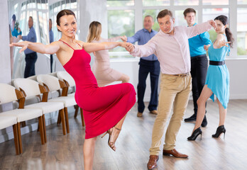 Positive adult pairs practicing vigorous jive movements in dance class