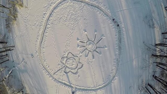 Kids run by path around sun and flower created on snow at winter