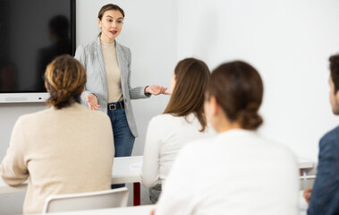 Naklejka na ściany i meble Young female tutor teaching students in college classroom