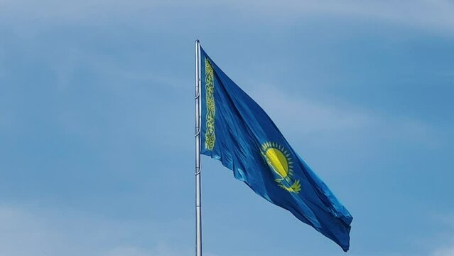 The flag of Kazakhstan is flying in the wind. Astana - Nur Sultan. A waving flag on a flagpole against the blue sky in Kazakhstan. The flagpole of the Republic of Kazakhstan on a bright sunny day. 4K 
