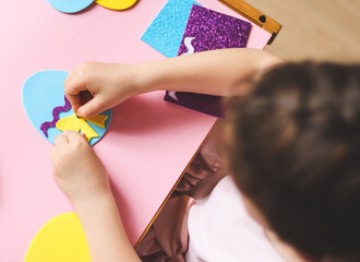 The hands of a little caucasian girl stick a yellow bow sticker on a felt egg