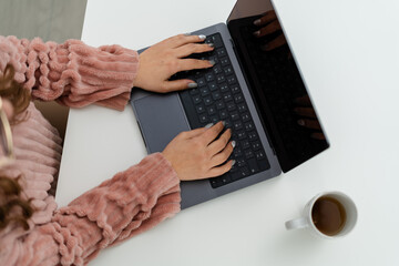 A top-down view of a person's hands typing on a modern laptop, with a cup of tea nearby on a white table, depicting a productive work session.