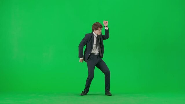 Portrait of male model in suit on chroma key green screen. Handsome young businessman in trendy suit dancing funny disco dance at the camera.