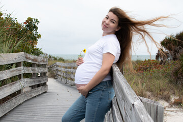 Happy pregnant Caucasian woman with a flower holding her baby bump. Third-trimester pregnancy