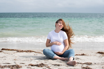 Fototapeta na wymiar Happy pregnant Caucasian woman sitting on a beach near the ocean. Happy pregnancy