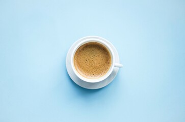 On a blue background there is a white cup with hot, aromatic, delicious cappuccino coffee. Flat lay, top view, close-up. Concept coffee break, hot drinks. Space for copying text.

