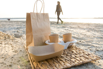 Eco-friendly beach picnic at sunset with paper cups, wooden cutlery, and plates on a woven mat. Minimalist, sustainable outdoor dining experience in a natural coastal setting.