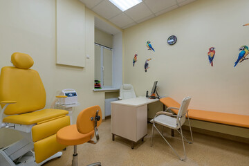 A children's doctor's office with bright orange examination chairs. Drawings of colored .birds on the wall.