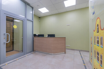 The bright lobby of the clinic with an entrance door and an information desk. The walls are decorated with drawings of houses.