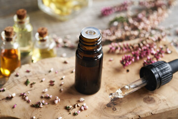 A glass bottle of aromatherapy essential oil with pink heather flowers